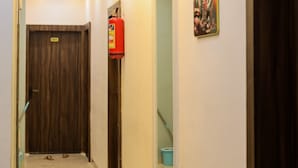 A hallway with a wooden door labeled "101", a fire extinguisher, a blue bucket, and a framed picture on the wall. - Hotel Shivganga (Ujjain)