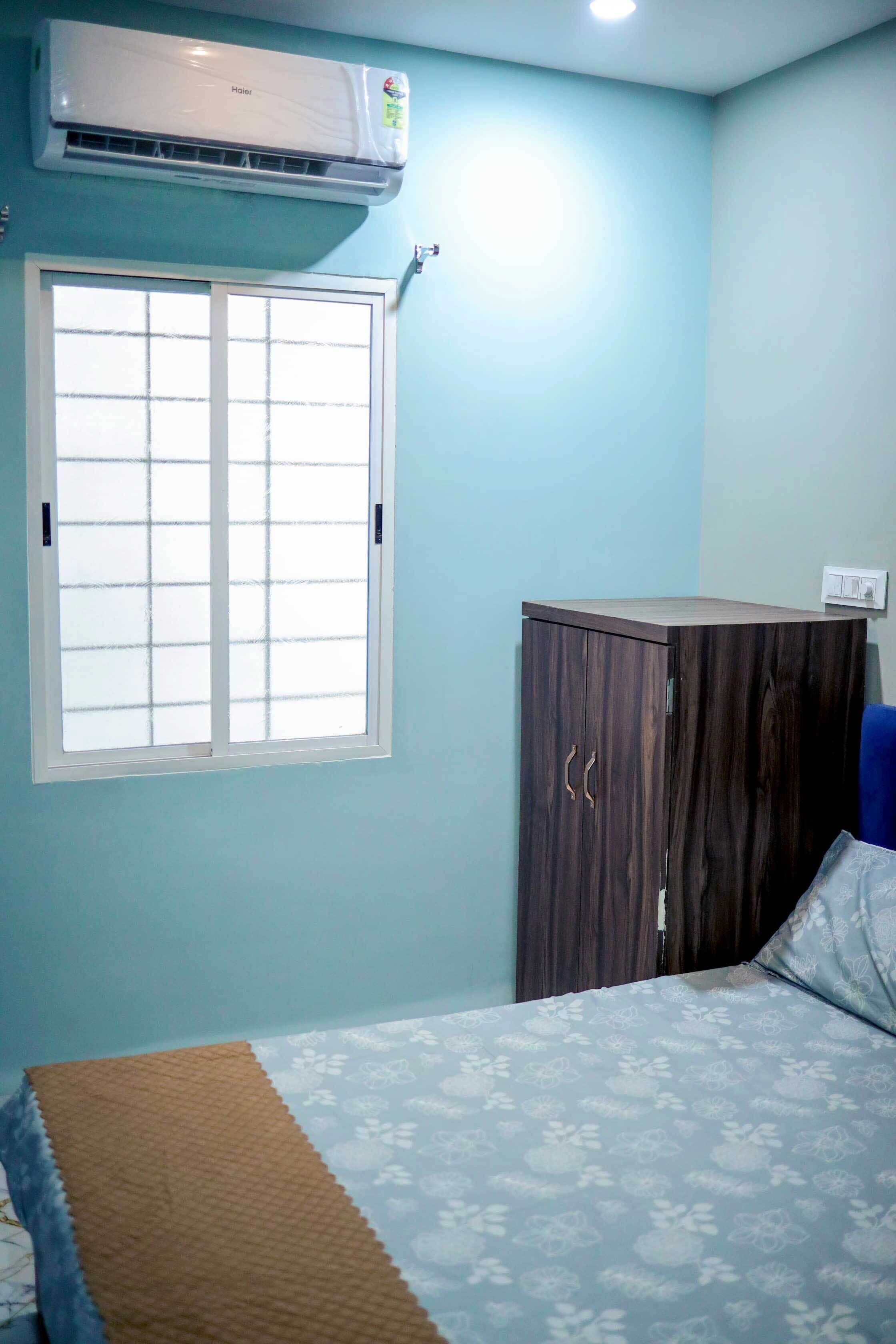 A room with a bed, a wardrobe, a window, and an air conditioner.