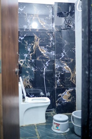 A bathroom with a toilet, a sink, and a marble wall. - Hotel Shivganga (Ujjain)