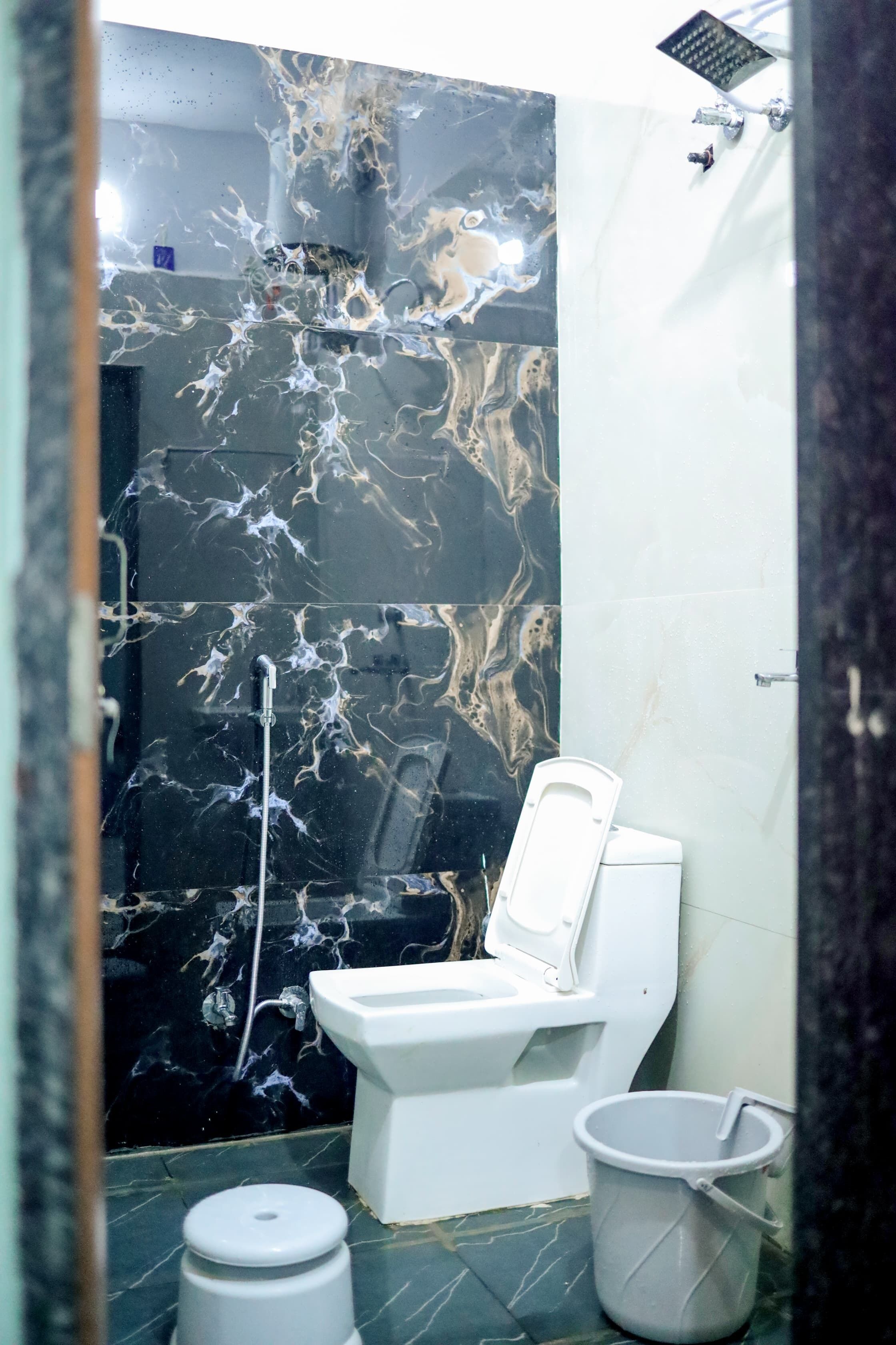 A bathroom with a black marble wall, a white toilet, and a white bucket.
