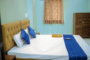 A neatly made bed with a blue quilt, a brown headboard, and a wooden wardrobe in a room with light blue walls. - Hotel Shivganga (Ujjain)