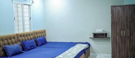 A bedroom with a bed, a wardrobe, a window, and an air conditioning unit.