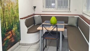 A dining area with a booth seating arrangement, a table with a green vase, and a window with a white curtain. - Vacation apartment Haus-Buxbaum near Lake Wörthersee (Sankt Martin am Techelsberg)