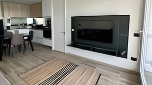 A modern living room with a large TV, a dining area with chairs, and a kitchen in the background. - Lagon, reef beach 414 (La Serena)