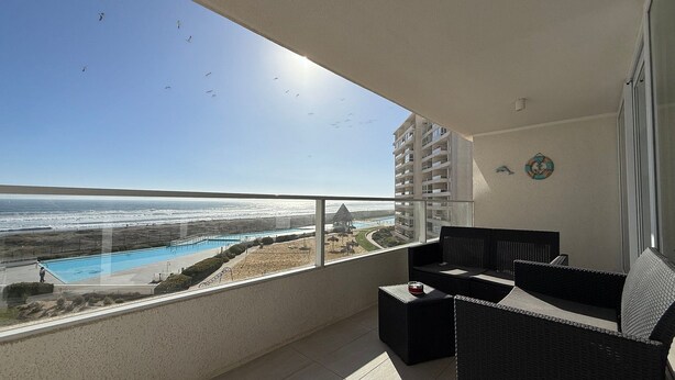 A balcony with a view of a swimming pool and beach, furnished with black wicker furniture, and a clock on the wall. - Lagon, reef beach 414 (La Serena)