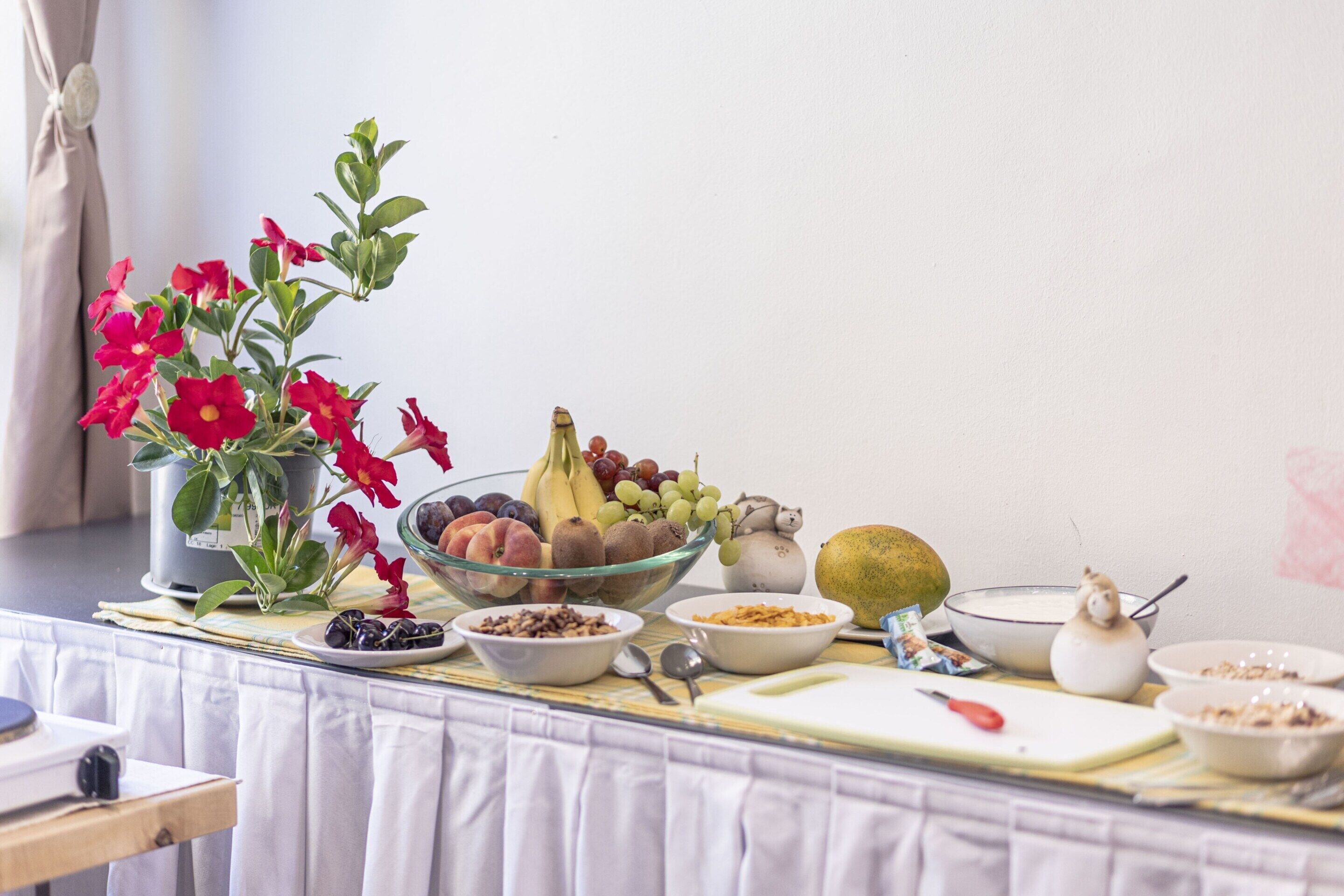 A breakfast table with various fruits, bowls of cereal, and a cutting board.