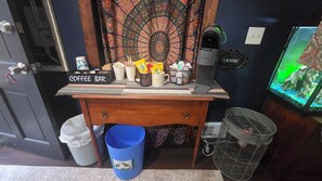 Zona de cafetería con máquina de café Keurig, un cesto de basura, un contenedor de reciclaje y un cartel de lavandería.