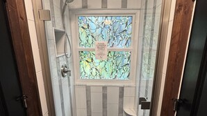 Un espace douche doté d’une porte en verre, d’un pommeau de douche et d’un panneau invitant les utilisateurs à réutiliser leurs serviettes.