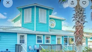A turquoise two-story building with a porch, a sign with a palm tree, and a palm tree in the foreground.