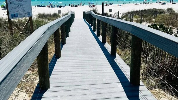 A wooden boardwalk leading to a beach with a sign indicating COVID-19 safety measures.