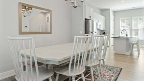 A modern kitchen with white cabinets, a stainless steel refrigerator, and a dining area with a white table and chairs. - One Tree Hill Townhouse - Downtown w/Garage! (Wilmington)