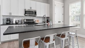 A modern kitchen with white cabinets, a large island with bar stools, a microwave, and a toaster. - One Tree Hill Townhouse - Downtown w/Garage! (Wilmington)