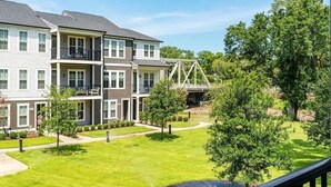A multi-story residential building with balconies, a well-maintained lawn, and a pedestrian bridge. - One Tree Hill Townhouse - Downtown w/Garage! (Wilmington)