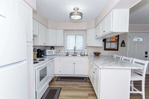 A modern kitchen with white cabinetry, a built-in microwave, a stove, and a dining area with white chairs.