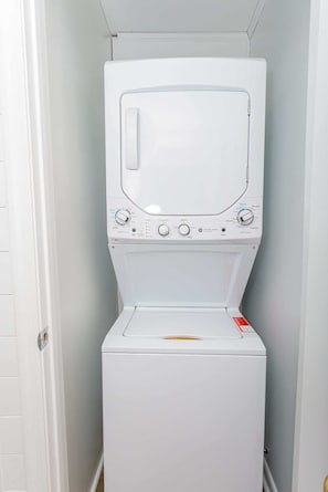 A front-loading white washer and dryer unit in a laundry room with a white door and light gray walls.