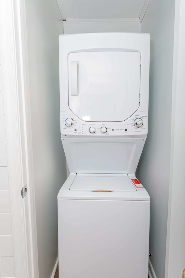 A front-loading white washer and dryer unit in a laundry room with a white door and light gray walls.