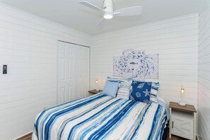A bedroom with a striped bedspread, a ceiling fan, a white door, and a wall-mounted artwork.