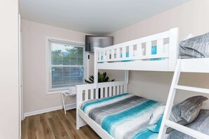 A bunk bed room with a window, a small table, and a plant.