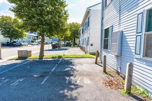 A residential street with parked cars, a sidewalk, and a row of houses with white siding and blue trim.