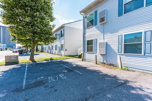 A row of white two-story townhouses with blue shutters, a parking lot, and a tree in the foreground.