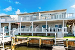 A multi-story waterfront property with balconies, a dock, and a grassy area.