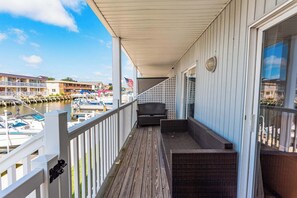 Ein Balkon mit Holzboden, einem Korbssessel und Blick auf einen Yachthafen mit Booten und einer Anlegestelle.