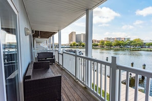 A covered balcony with wicker furniture, a view of a river, and buildings in the background.