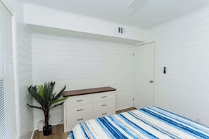 A bedroom with a bed, a dresser, a potted plant, and a door.