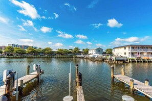 A waterfront dock with a wooden pier extending into calm water, surrounded by buildings and trees.