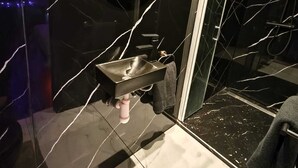 Ett badrum med en vägg av svart marmor, en rund spegel, ett handfat och en duschhörna.