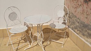 A small outdoor patio with a round table and two chairs, a tiled floor, and a plain wall.