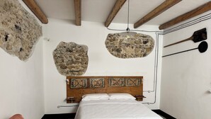 A bedroom with a wooden headboard, a bed with white bedding, a stone wall, and a stone shelf.