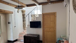 A room with a wooden staircase, a television mounted on the wall, a wooden door, and a vintage sewing machine on a small table.