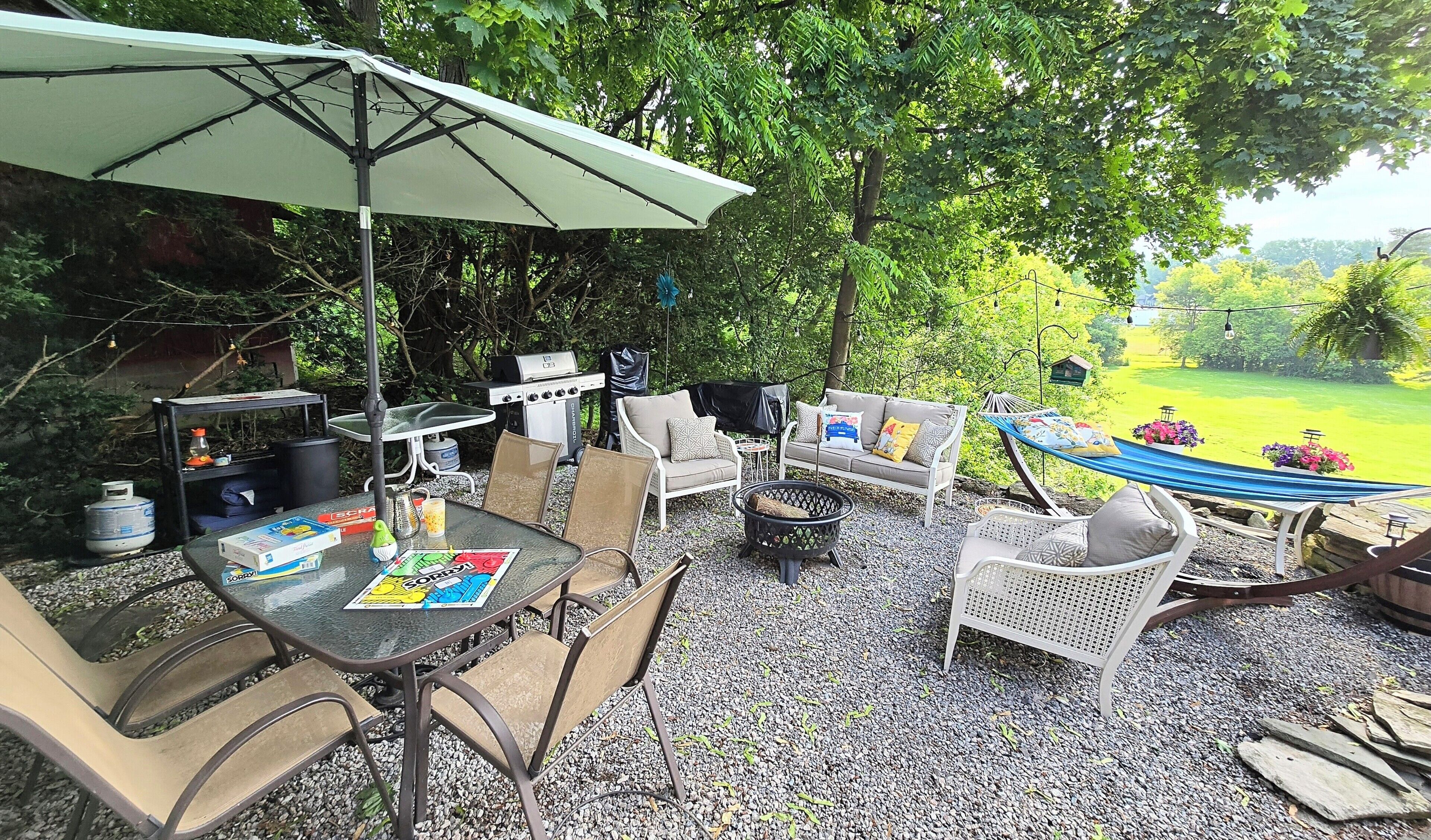 Un patio al aire libre con mesa, sillas, una parrilla y una hamaca.