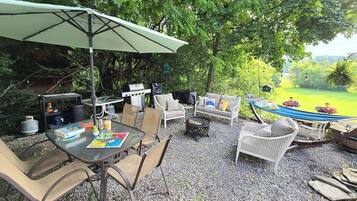 Un patio al aire libre con mesa, sillas, una parrilla y una hamaca.