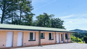 A brick building with multiple doors, a gravel driveway, and trees in the background. - Motel Room 1A with Bar & Grill and Laundromat (Copperhill)