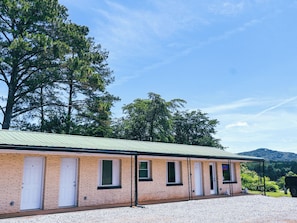 A brick building with multiple doors, a gravel driveway, and trees in the background.
