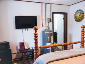 A bedroom with a bed, a TV mounted on the wall, a heater, and a wooden chair.