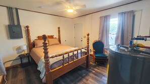 A bedroom with a four-poster bed, a chair, a desk with a water heater, and a window with curtains.