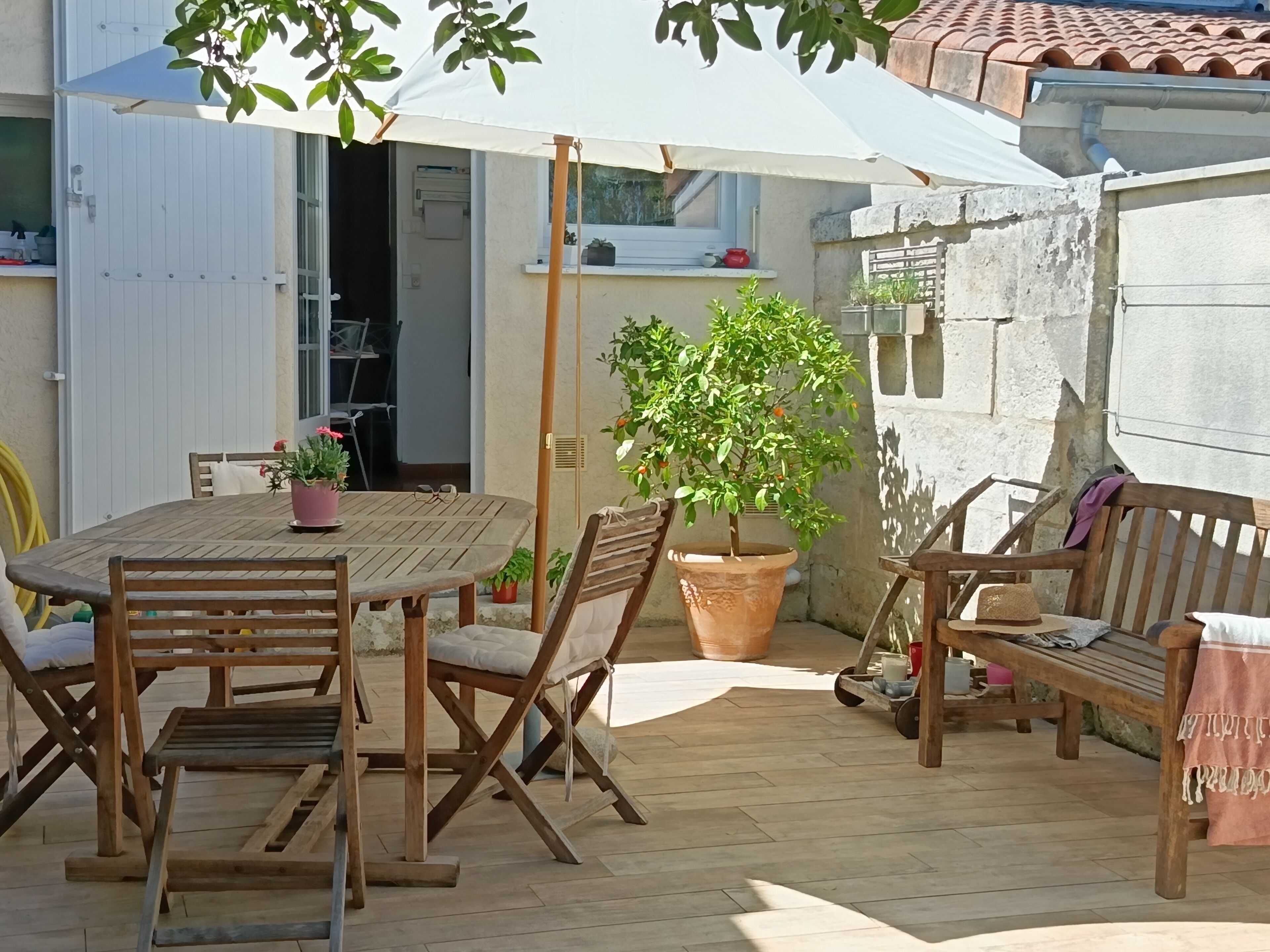 Een terras buiten met een houten tafel en stoelen, een grote parasol en een potplant.