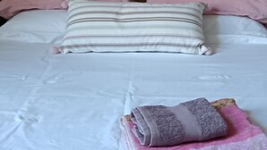 Un lit avec des oreillers roses et blancs, un oreiller à rayures et une serviette enroulée sur un couvre-lit blanc.