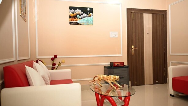 A modern living room with a glass coffee table, red and white sofas, a leopard figurine, and a framed picture on the wall. - The Travellers Club (Guwahati)