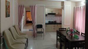 A spacious living room with a dining area, kitchen, and a bedroom with a door leading to another room. - The Travellers Club (Guwahati)