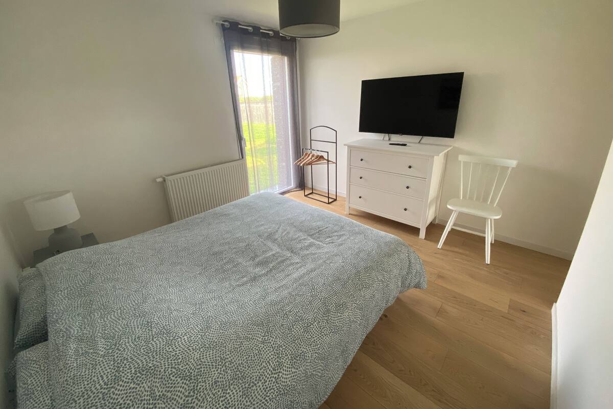Un dormitorio con una cama, un tocador, un televisor, una silla y una ventana con cortinas.