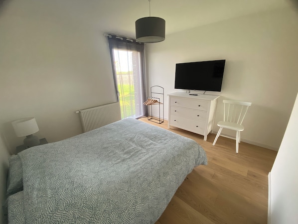 Un dormitorio con una cama, un tocador, un televisor, una silla y una ventana con cortinas.