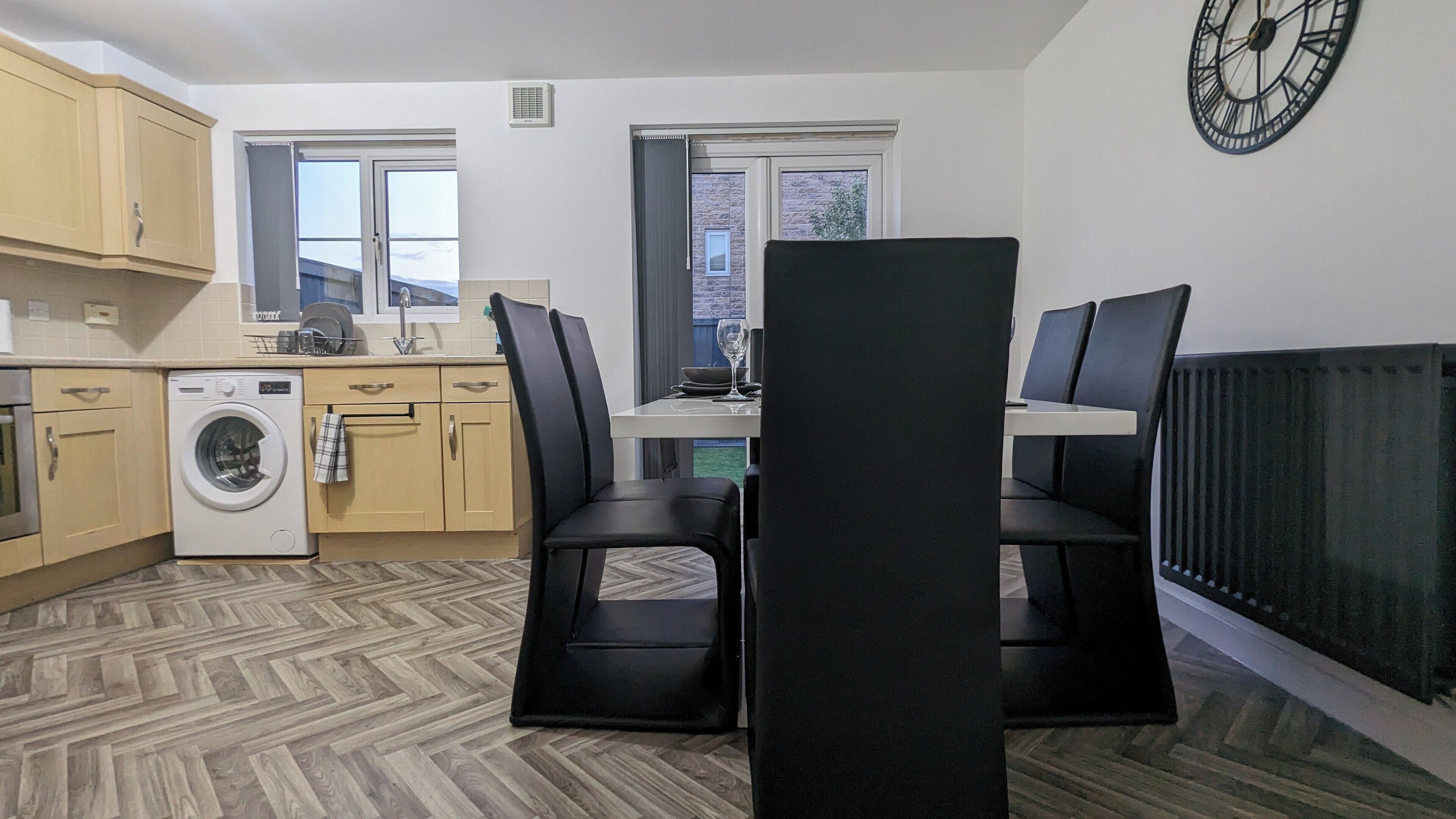 A compact kitchen with a washing machine, wooden cabinets, and a dining area with black chairs.