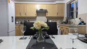 A modern kitchen with wooden cabinets, a stainless steel range hood, and a dining area with a table set for two. - Leyland Road Retreat - 4 Bedroom House (Burnley)