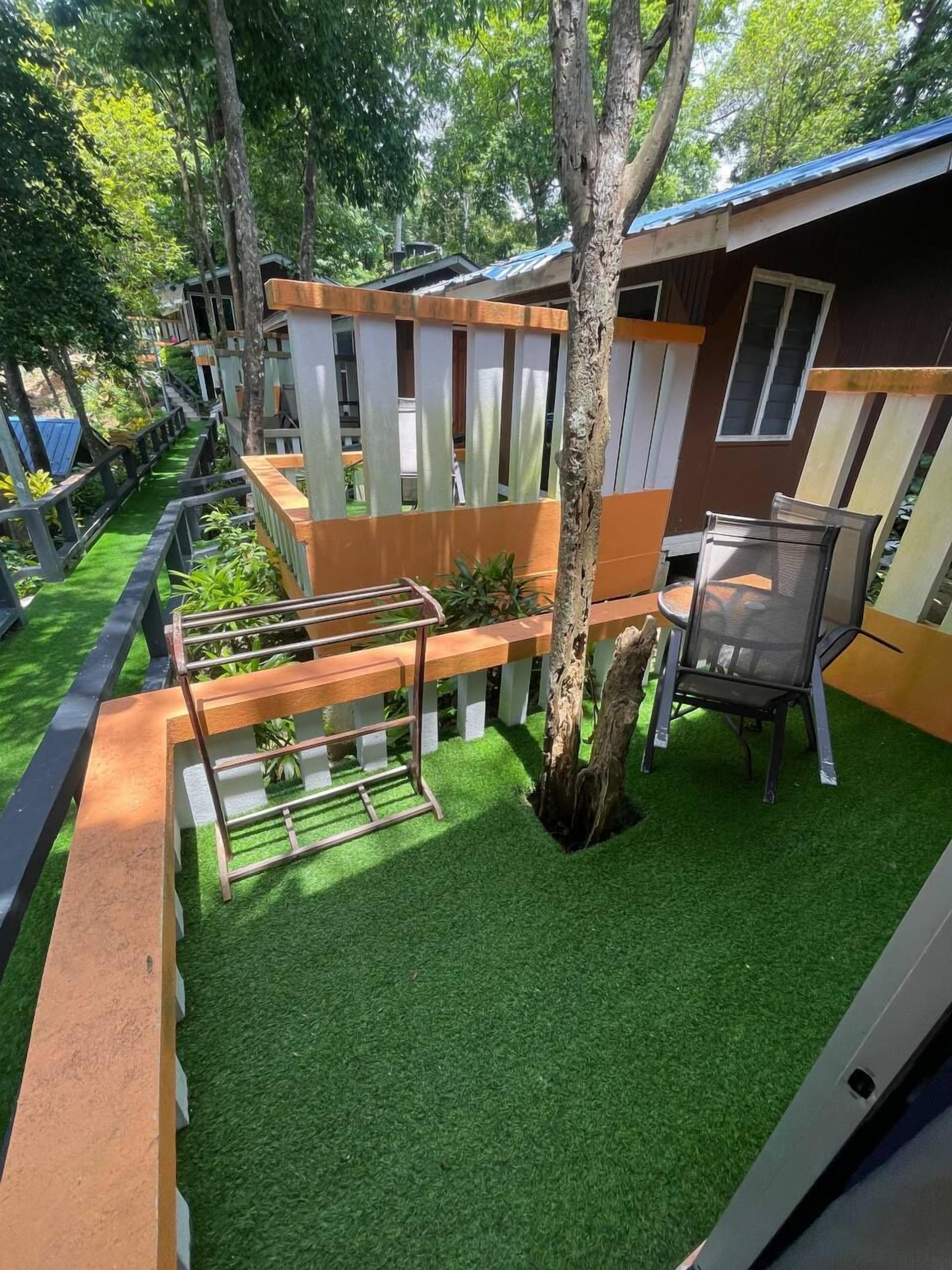 A modern outdoor area with artificial grass, a wooden bench, a metal chair, and a tree.