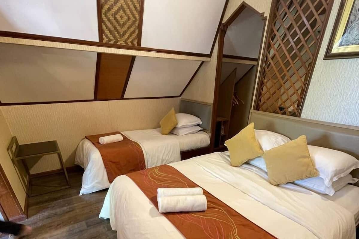 Quarto de hotel com duas camas, piso de madeira e um painel decorativo na parede.
