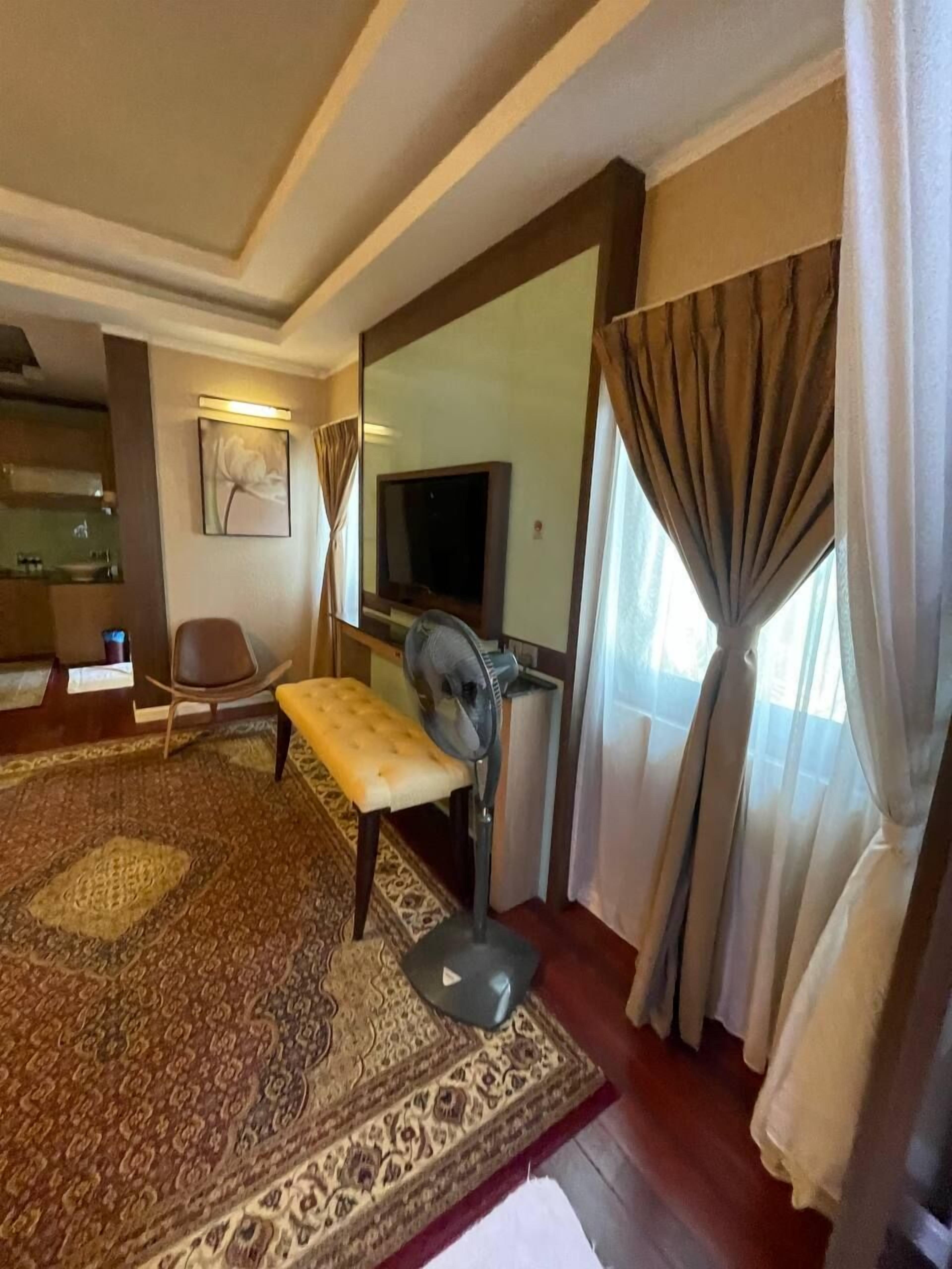 Une chambre d’hôtel avec un grand tapis à motifs, un banc, un ventilateur, une télévision et un miroir.